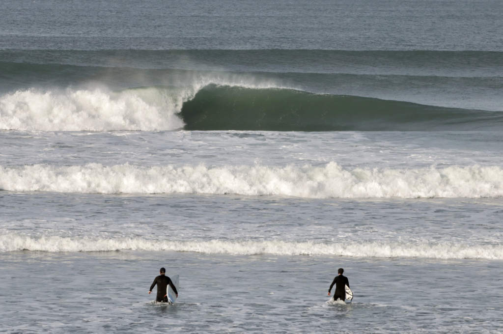 Ocean Beach Wave with 2 surfers in wetsuits walking out to the surf